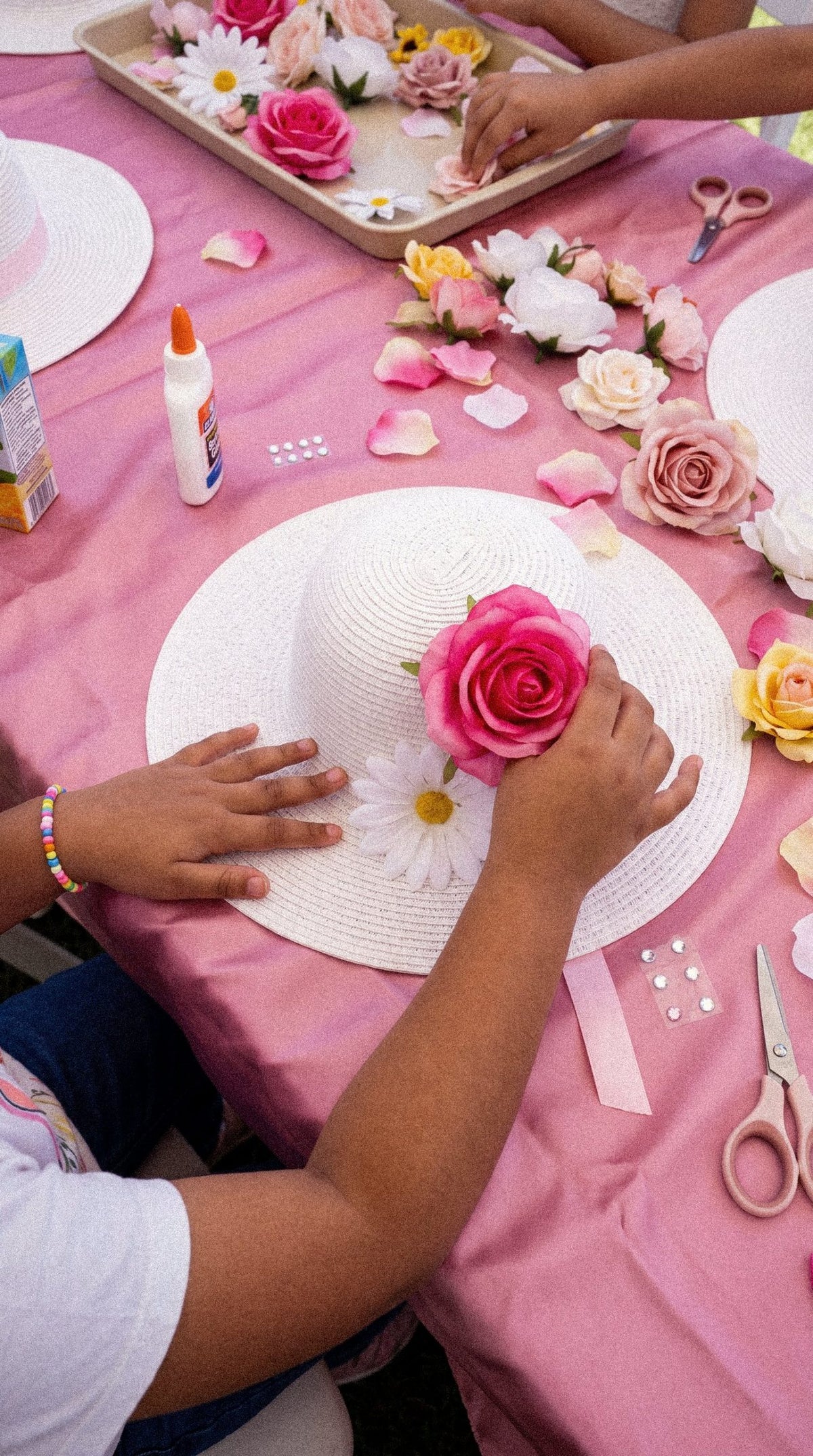 A child adding a rose to a white straw hat
