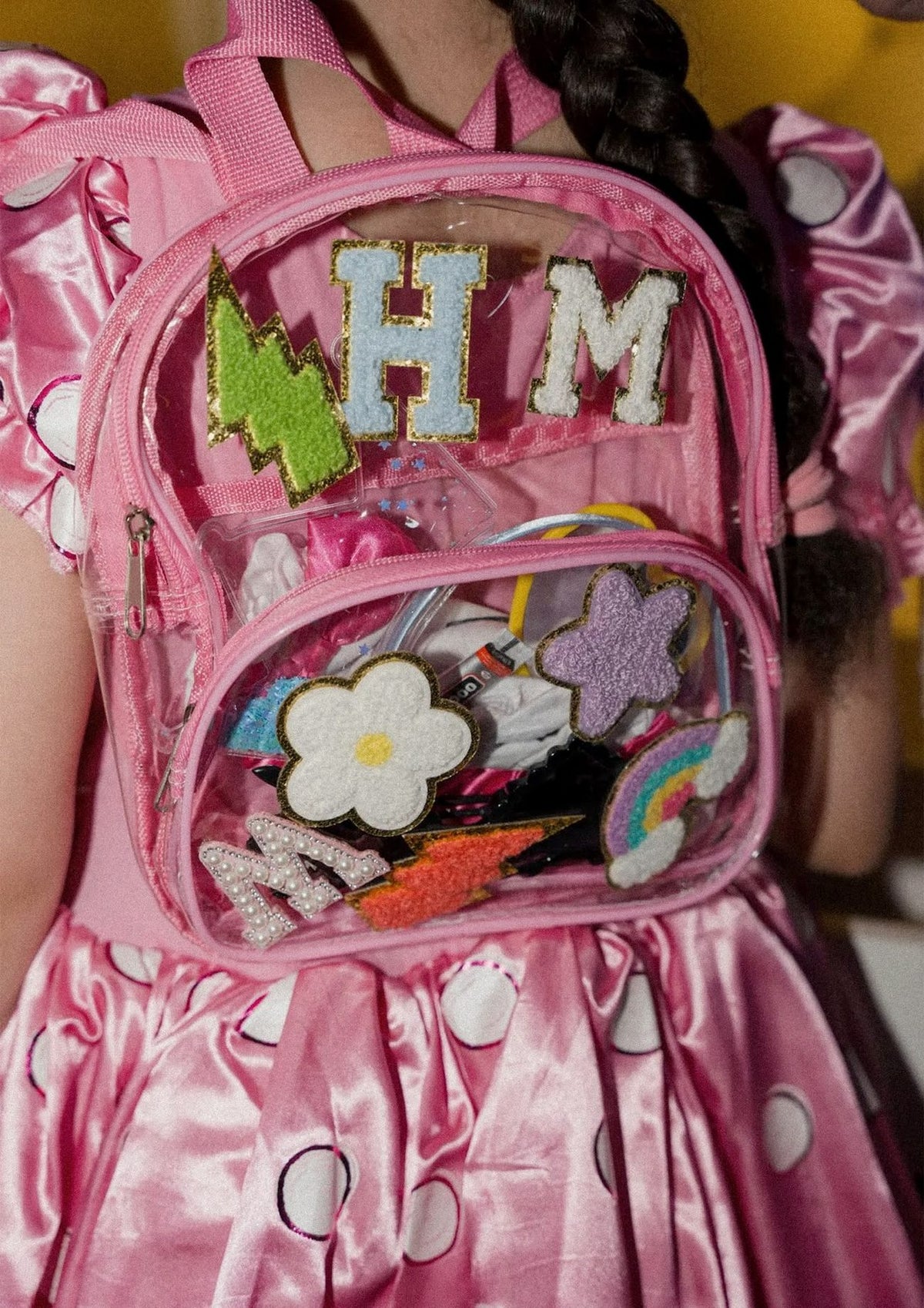 A child wearing a clear backpack decorated with patches